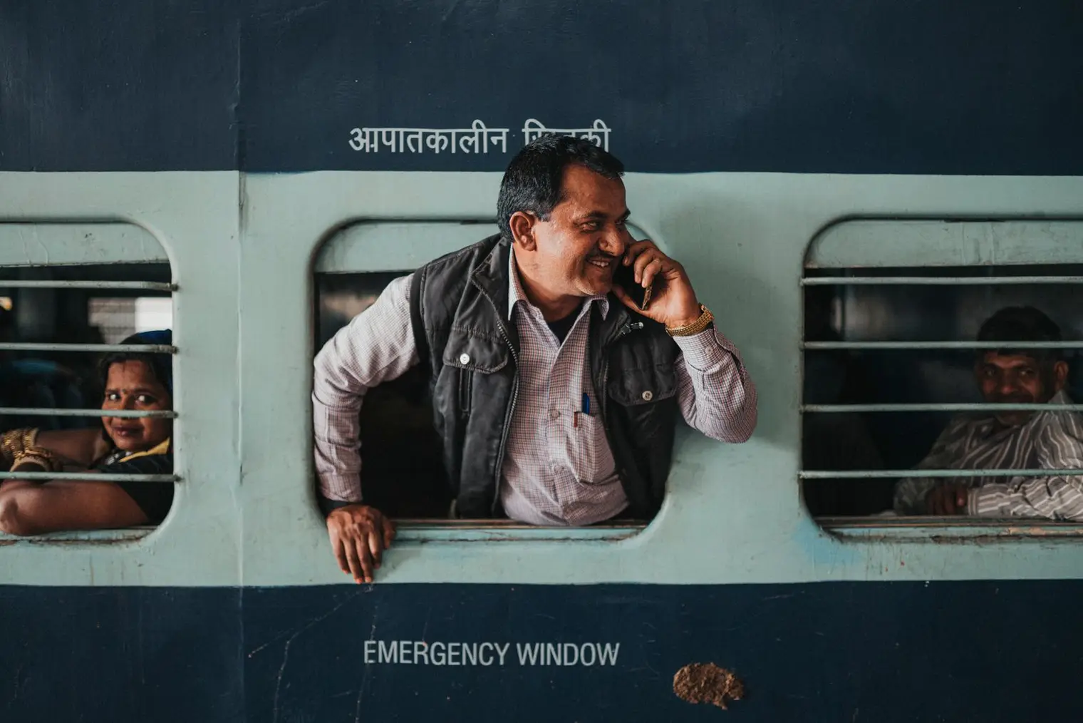 A smiling man talks on his mobile phone while leaning out of a train window in Jaipur, Rajasthan