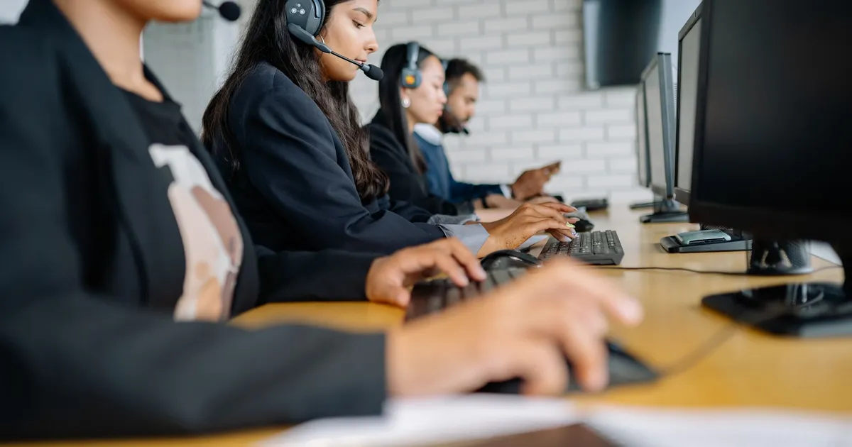 A row of call centre agents wearing headsets, working at computers on a long desk